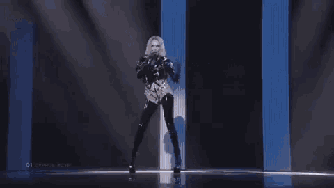 a woman is singing into a microphone on a stage in front of a blue and white wall .