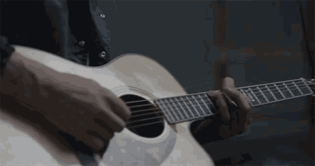 a man is playing an acoustic guitar with his hands on the strings