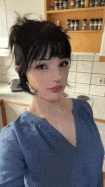 a woman in a blue shirt is standing in a kitchen
