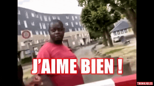 a man in a red shirt stands in front of a sign that says j'aime bien !