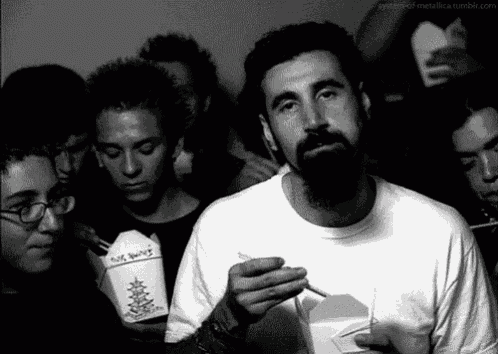 a man with a beard is smoking a cigarette while holding a box of noodles