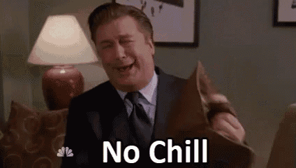 a man in a suit and tie is sitting on a couch holding a pillow and laughing .
