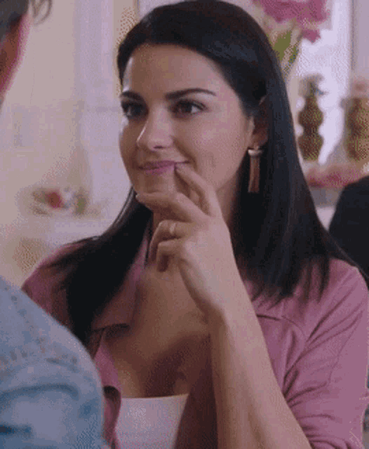 a woman in a pink jacket is smiling with her hand on her face