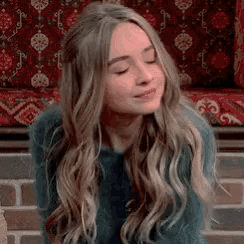 a woman with long blonde hair is wearing a green sweater and smiling .