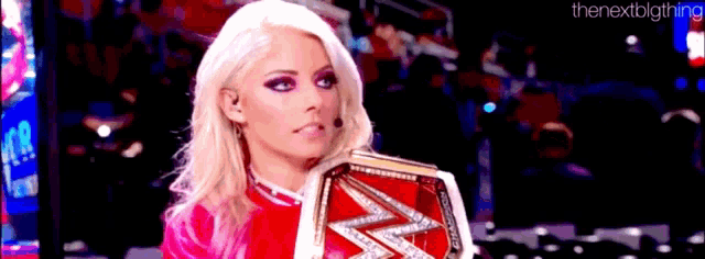 a woman in a pink dress is holding a wrestling championship .