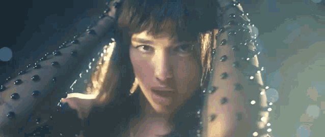 a close up of a woman 's face in a dark room . she is wearing a black polka dot dress .