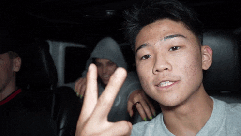 a young man giving a peace sign while another man looks on
