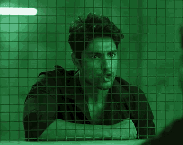 a man behind a wire fence with a green light behind him