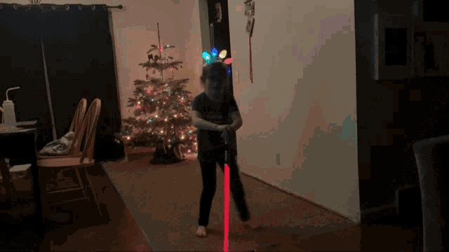 a little girl holding a red lightsaber in front of a christmas tree