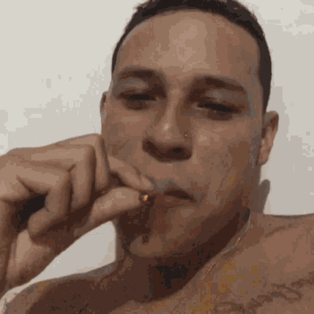 a shirtless man is smoking a cigarette with a tattoo on his arm that says " jesus "