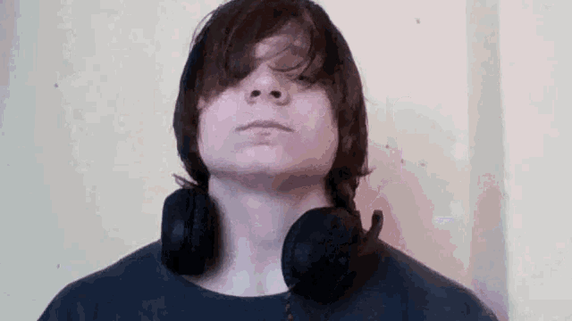 a young man with headphones around his neck looks at the camera with his eyes closed