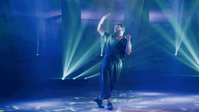 a man in a black jumpsuit is dancing on a stage with green lights behind him
