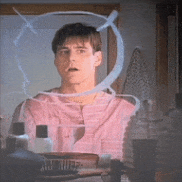 a man in a pink shirt is looking in a mirror