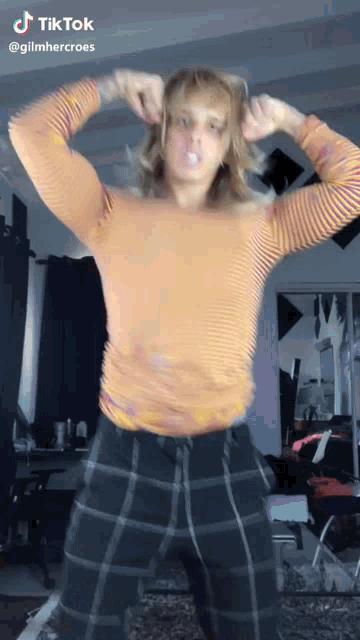 a woman in a striped shirt and plaid pants is dancing on tik tok