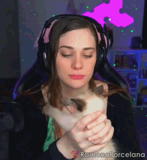 a woman wearing headphones is holding a small kitten in her arms