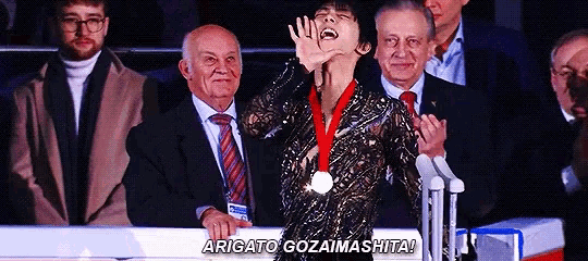 a man wearing a medal stands in front of a crowd and says " arigato gozaimasita "