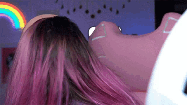 a woman with pink hair is laying on a pink couch with a rainbow in the background .