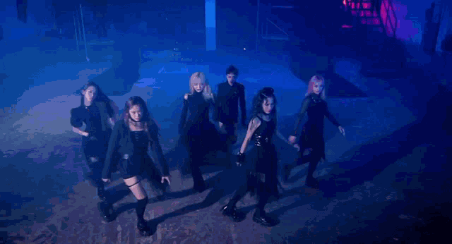 a group of dancers are performing on a stage in a dark room with purple lights .