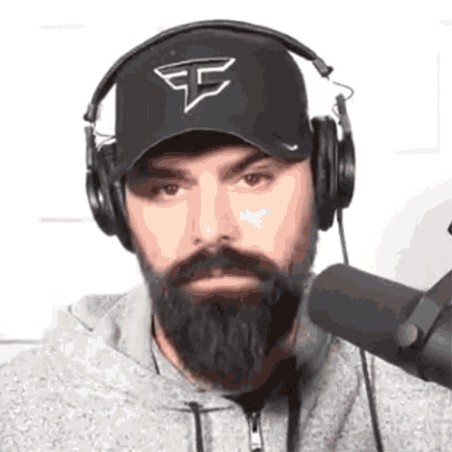 a man with a beard is wearing headphones and a hat with the letter e on it .