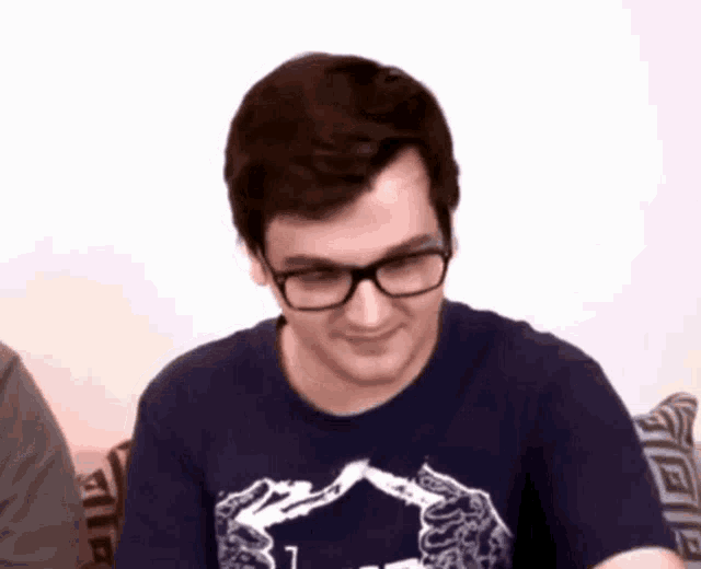 a man wearing glasses and a blue t-shirt is smiling .
