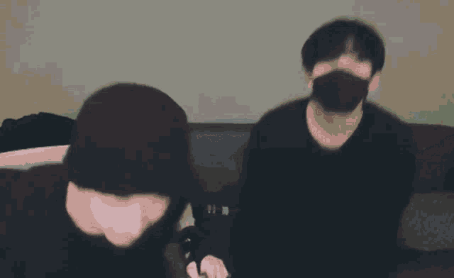 a man wearing a mask is sitting on a couch with another man