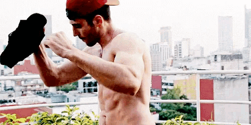a shirtless man is standing on a balcony holding a pair of shoes