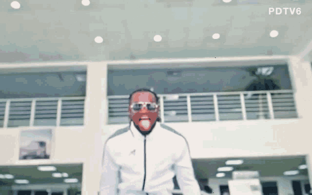 a man wearing sunglasses and a white jacket is standing in front of a building with the letters pdtv6 on the bottom