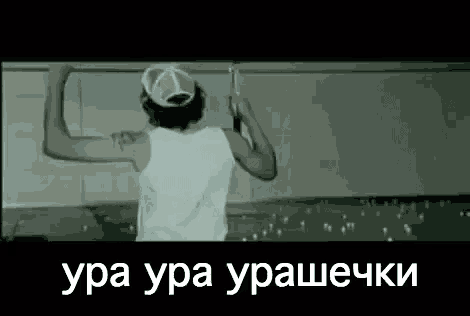 a man wearing a hat and a white tank top is standing in front of a wall with his arms outstretched .