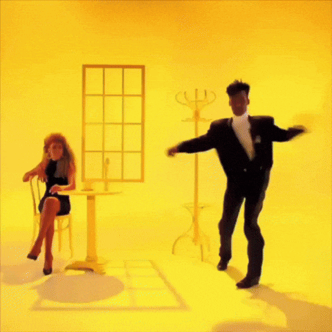 a man in a suit and tie is dancing next to a woman in a chair