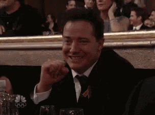 a man in a tuxedo and tie is smiling while sitting in a crowd .