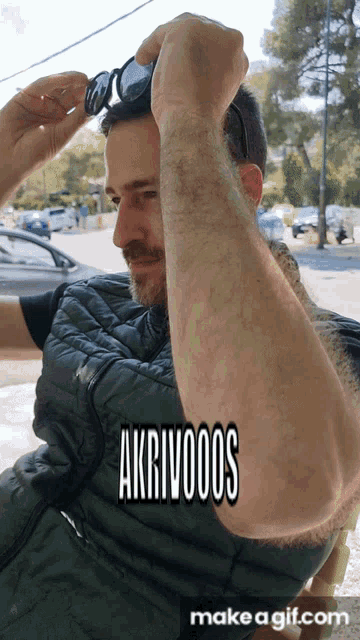 a man adjusts his sunglasses while wearing a green vest with the words akrivooos on it