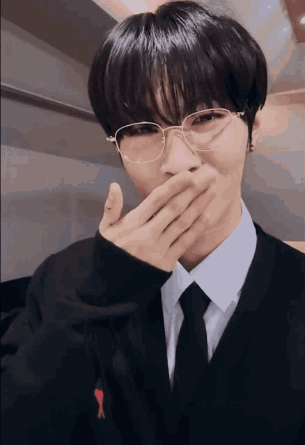 a man wearing glasses and a black sweater covers his mouth