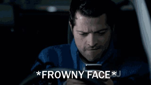 a man sitting in a car looking at a cell phone with the words * frowny face * written above him