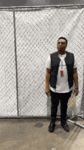 a man is standing in front of a chain link fence wearing a vest .