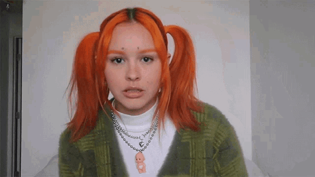 a girl with red hair and pigtails is wearing a green sweater