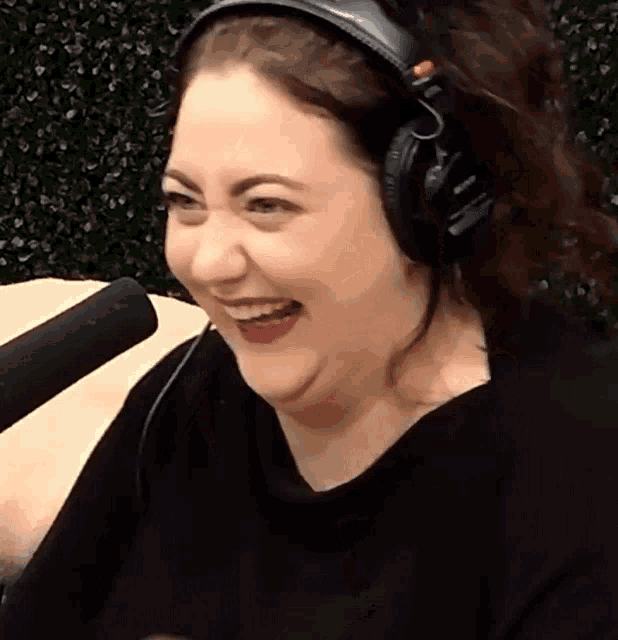 a woman wearing headphones and a black shirt is smiling in front of a microphone
