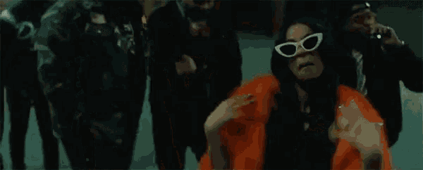 a group of people are standing around a woman in a fur coat and sunglasses .