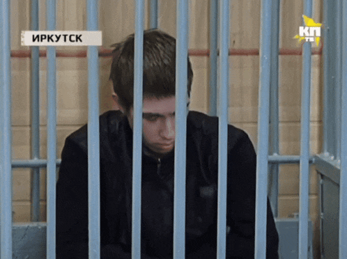 a man sits in a jail cell with a sign that says ' irkutsk ' on it