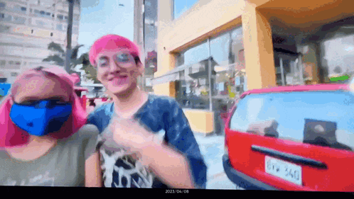 a man and a woman wearing face masks are standing in front of a red car ..