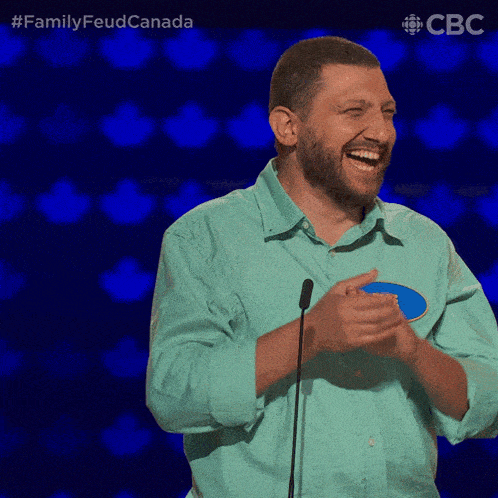 a man in a blue shirt applauds in front of a microphone with the words family feud canada on the bottom