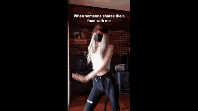 a woman wearing a hat and a mask is dancing in front of a brick wall ..