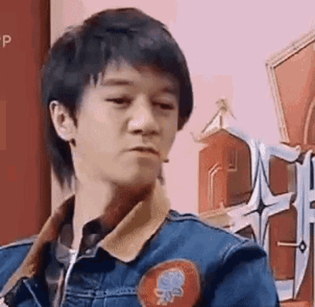 a young man wearing a denim jacket with a patch on it is making a funny face .