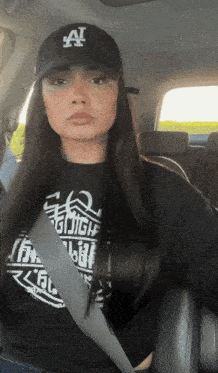 a woman wearing a black hat with the letter a on it sits in a car