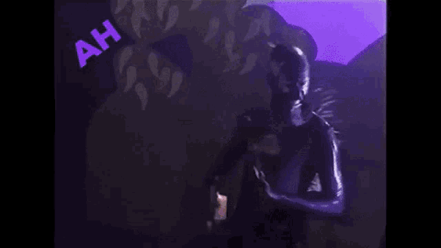 a person is standing in a dark room with a purple background and a purple sign that says ah .