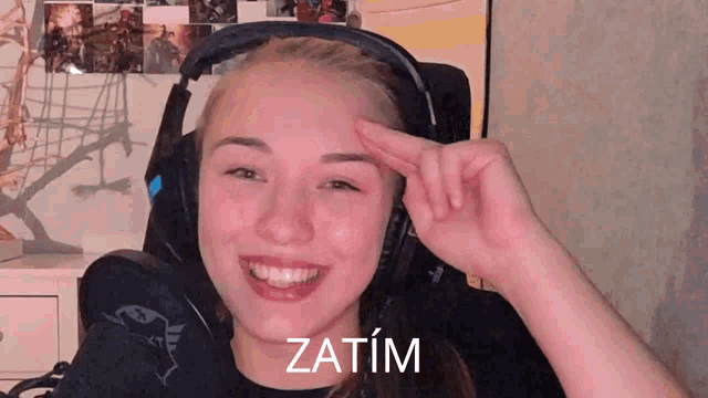 a woman wearing headphones is smiling with the word zatim written on her forehead
