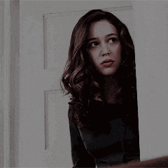 a woman holds her finger to her lips while peeking out of a doorway .