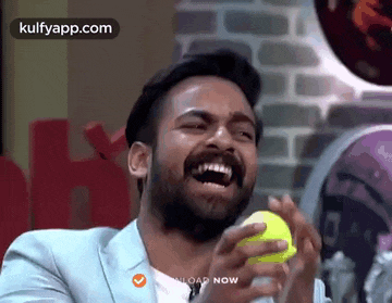 a man with a beard is laughing while holding a tennis ball in his hands .