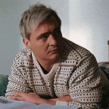 a man wearing a sweater is laying on a bed with his hands folded