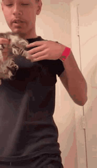 a man in a black shirt is holding a kitten in his hand