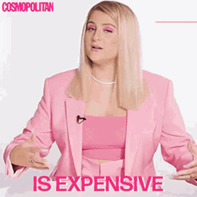 a woman in a pink suit is sitting at a table with a microphone .